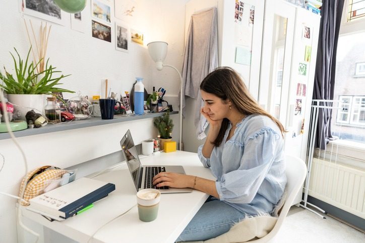 a young woman sits at her desk in her dorm room studying