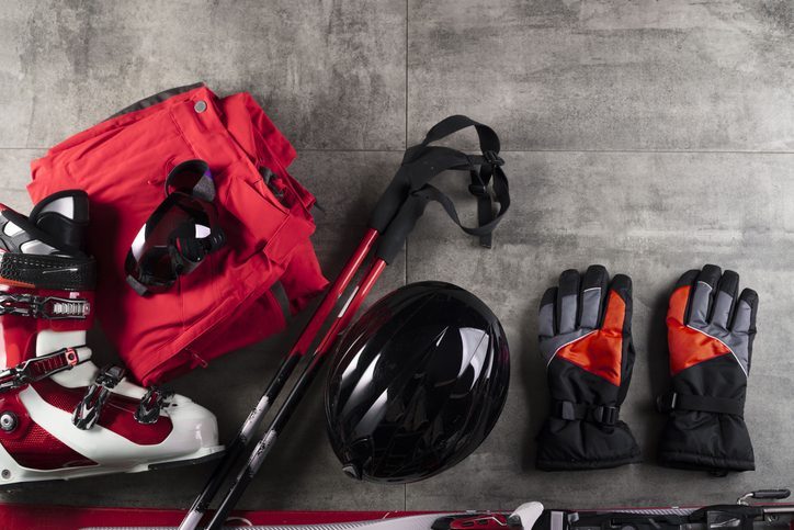Ski boots, gloves, poles, and a helmet laying on cement.