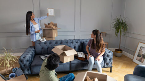Three people around sitting around a couch unpacking boxes