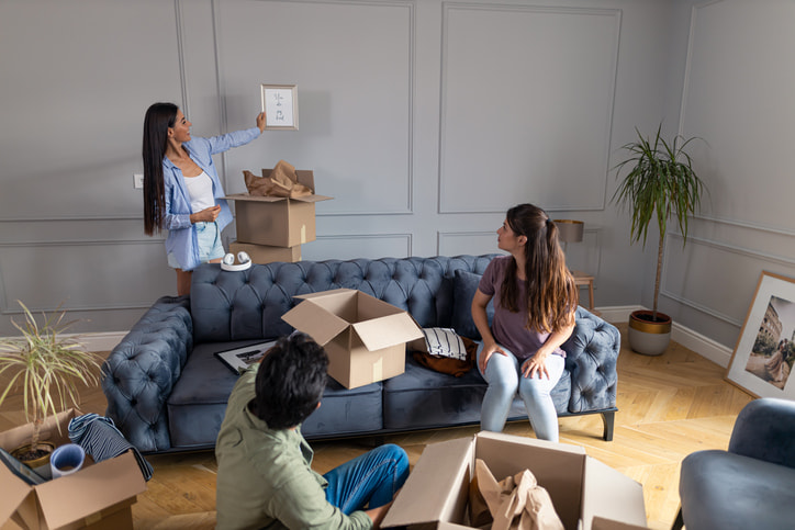 Three people around sitting around a couch unpacking boxes