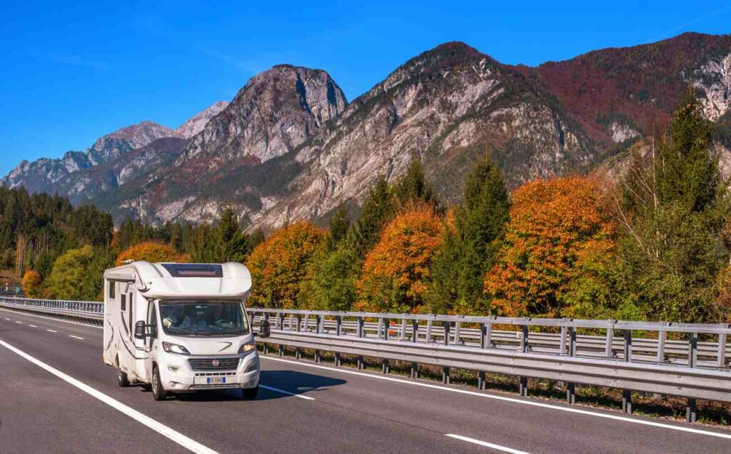 A white RV driving down the road with trees and mountains in the background