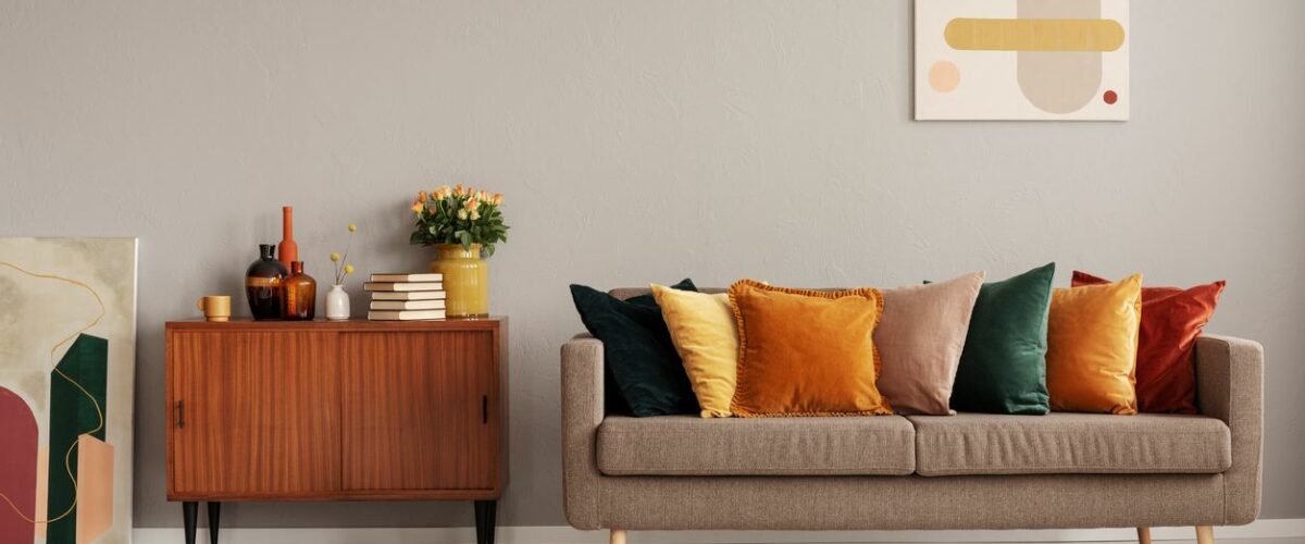 A living room with a couch, colorful pillows, a console table, and a yellow knit ottoman