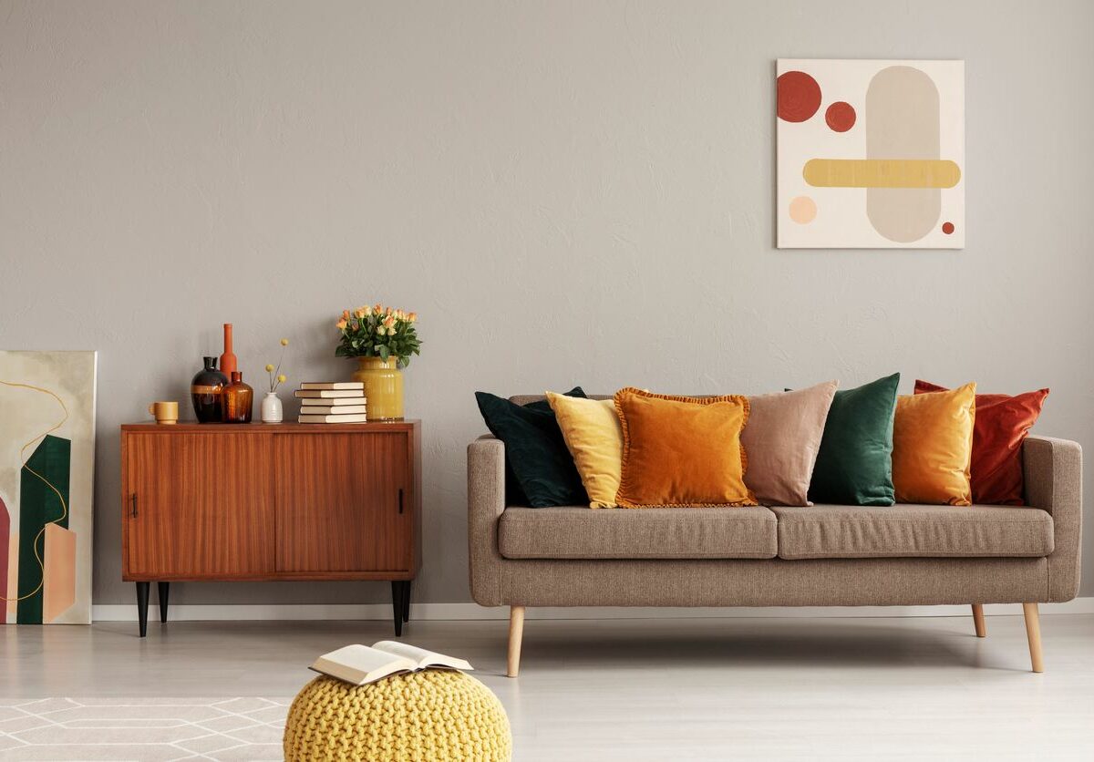 A living room with a couch, colorful pillows, a console table, and a yellow knit ottoman