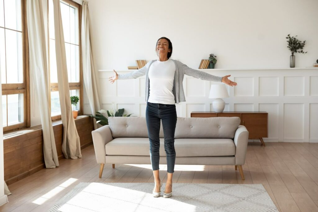 A happy woman standing in her apartment with her arms stretched out