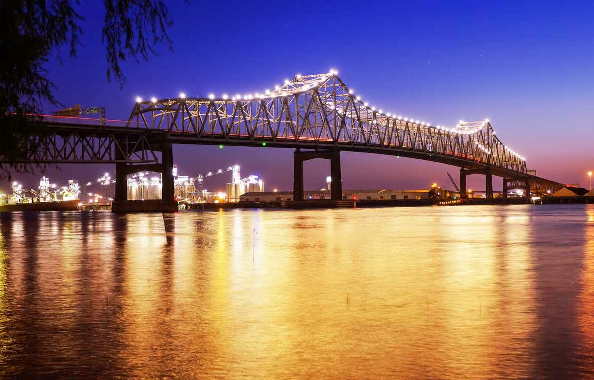 A well-lit bridge stretches over a river in front of a city