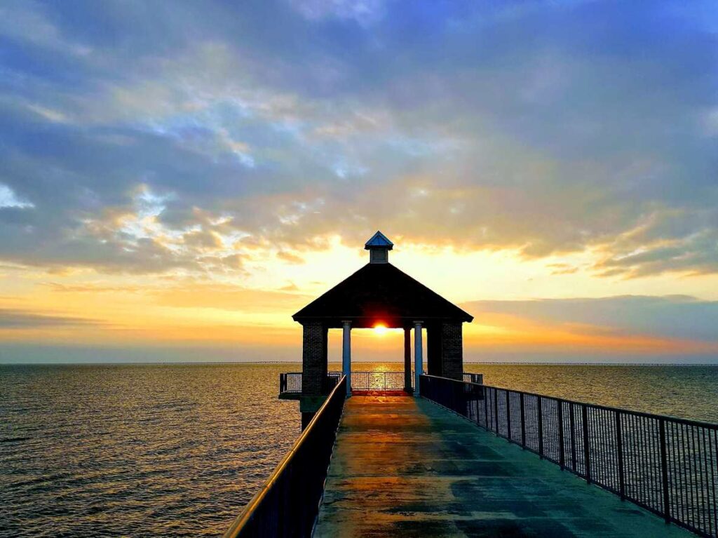 A boardwalk with a small gazebo extends into open water at sunset.