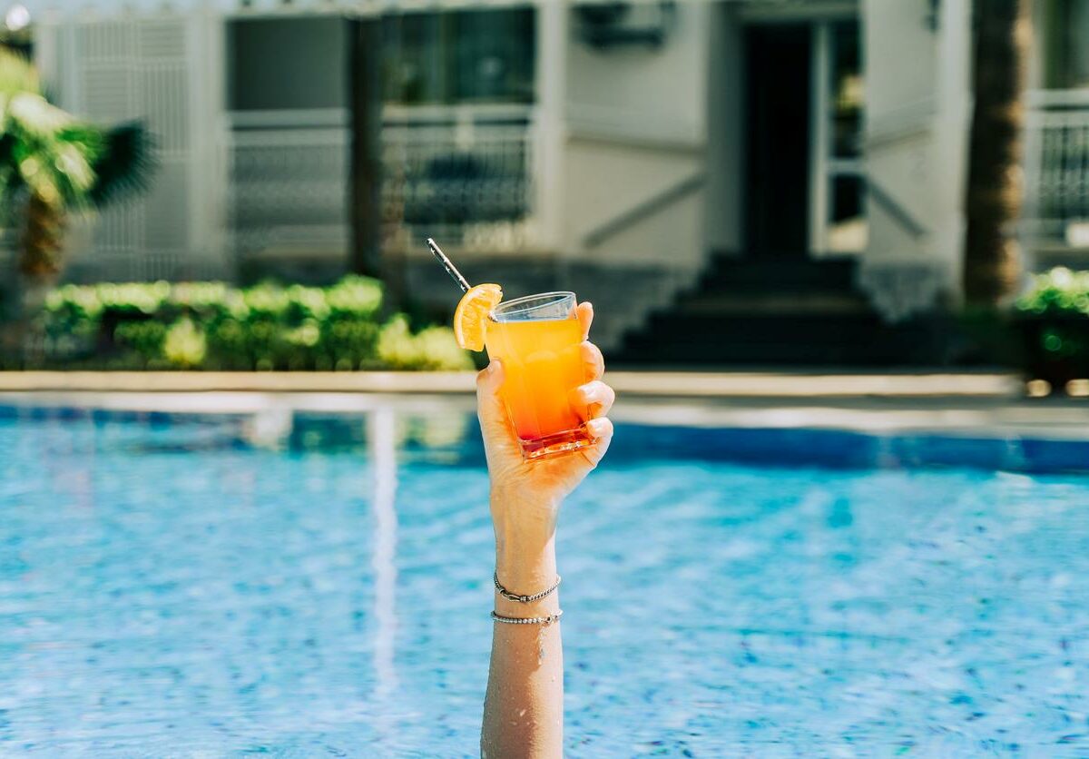 Closeup woman's hand sticking out of the swimming pool holding a tropical cocktail.