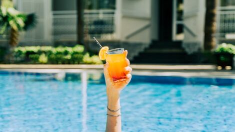 Closeup woman's hand sticking out of the swimming pool holding a tropical cocktail.