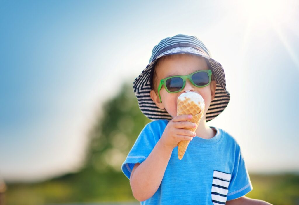 A child eats ice cream outdoors on a bright sunny day.