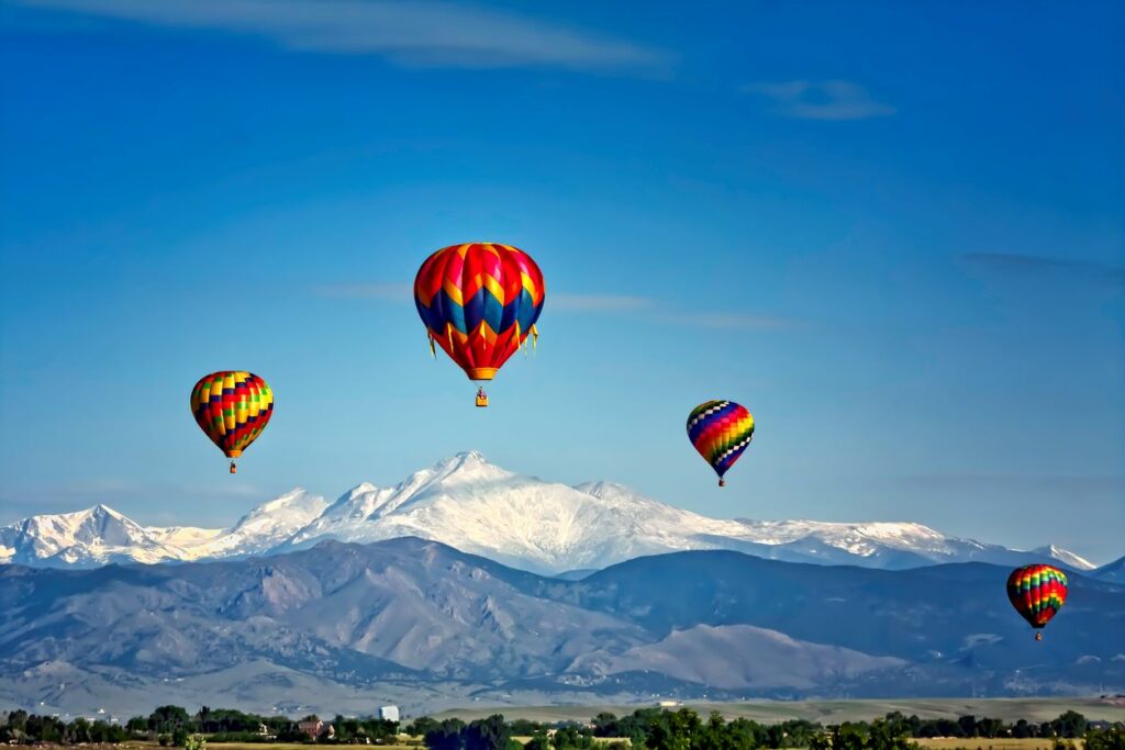 Four colorful hot air balloons floating in front of a snowy mountain