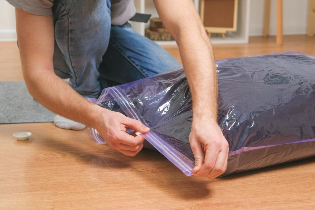 Man uses a vacuum bag to store away clothing.