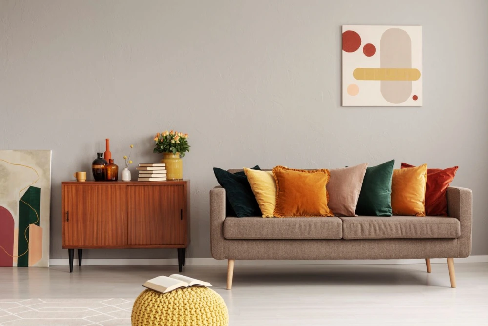 A living room with a couch, colorful pillows, a console table, and a yellow knit ottoman