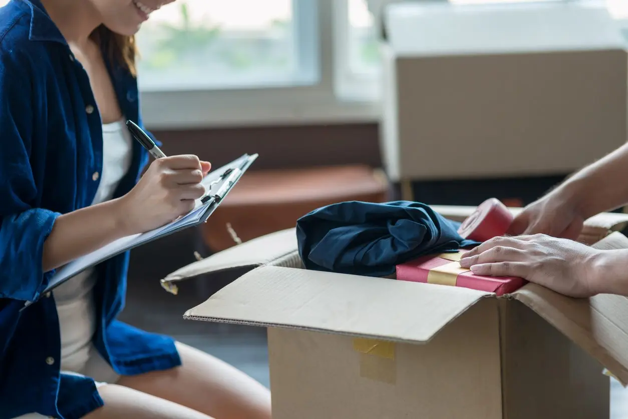 A young couple packing and checking items into a storage box before moving to a new home.