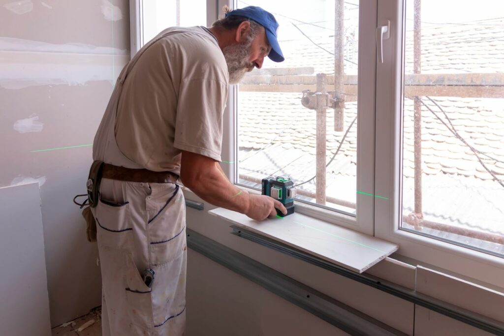 A male contractor works on renovating the windowsill of a home.