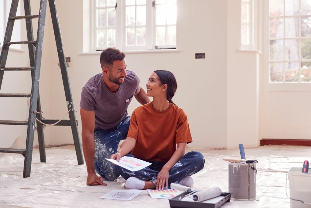 A man and woman sitting on the floor surrounded by paint while renovating a room.