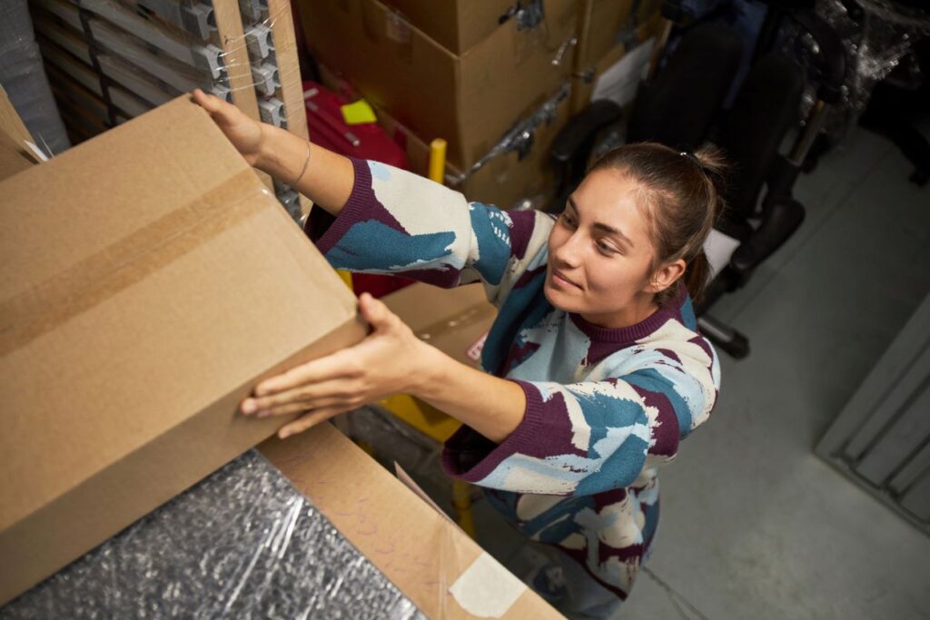 A young woman storing belongings on a high shelf inside of a storage unit. 