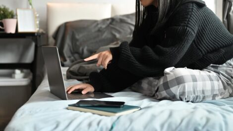 A college student working on homework in bed.