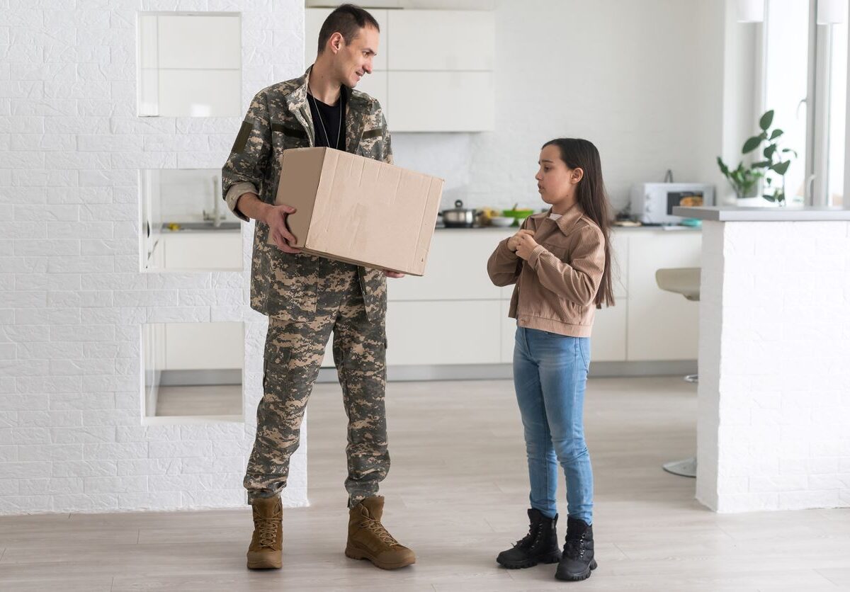 A military dad holding a box for storage and standing with his daughter.