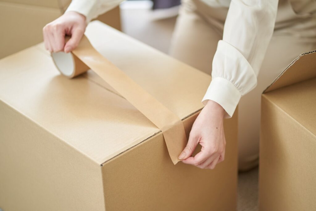 A woman sealing a cardboard box with tape, preparing items for long-term storage. 