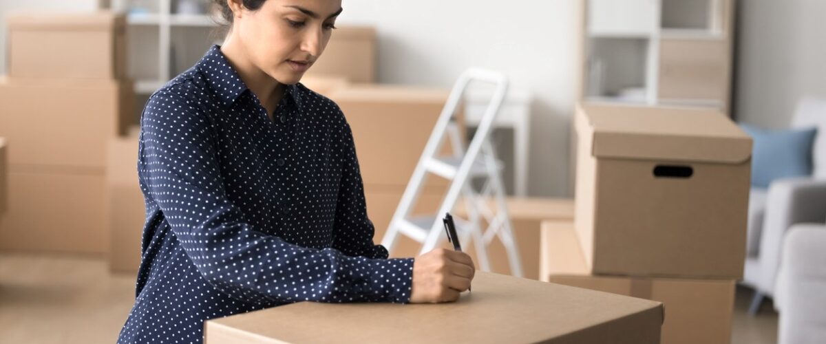 A woman labeling a cardboard box in her living room.