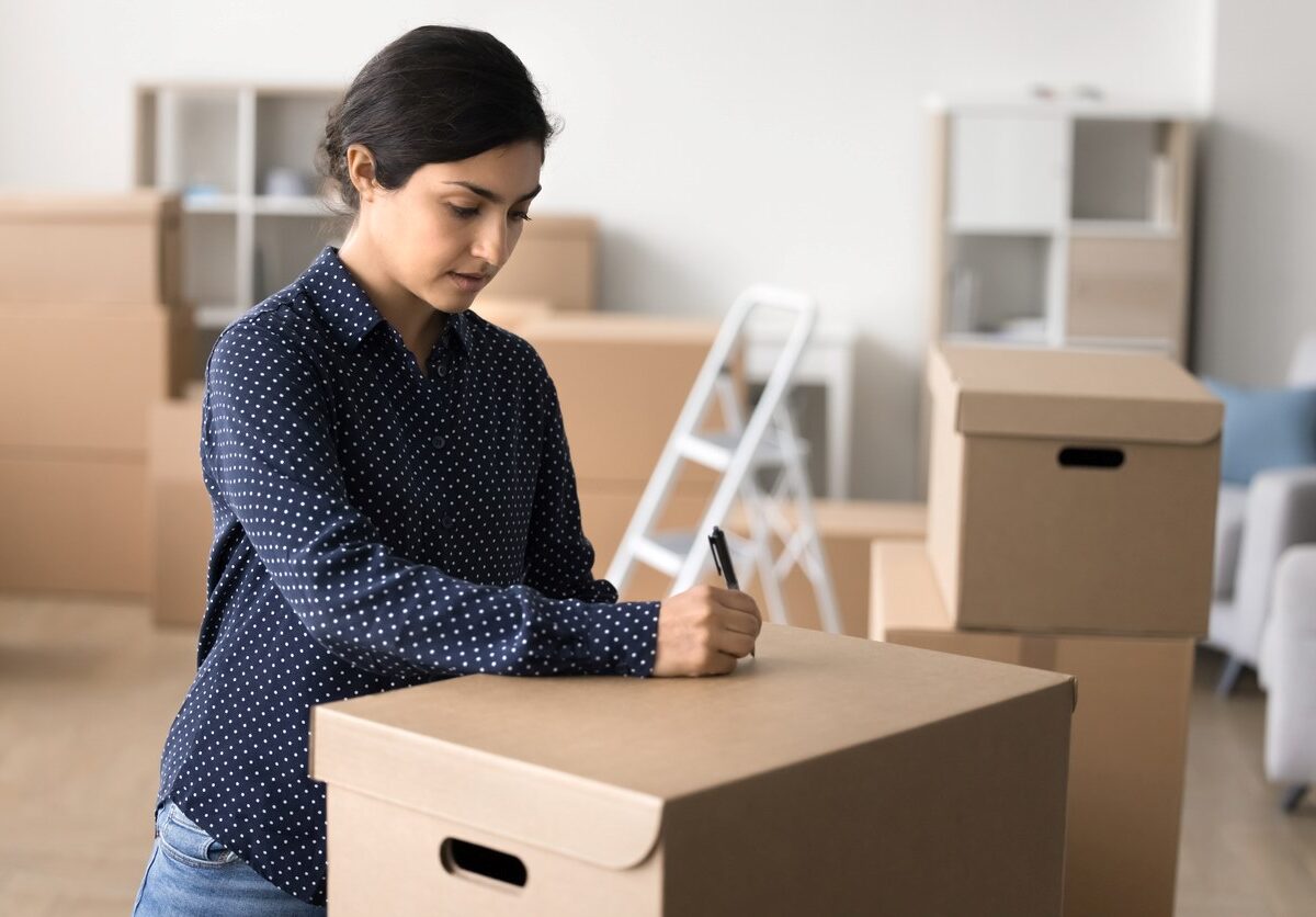 A woman labeling a cardboard box in her living room.