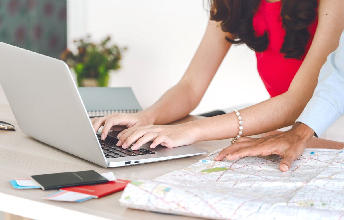 Two people planning travel using a laptop and a map, with passports and notebooks on the table.