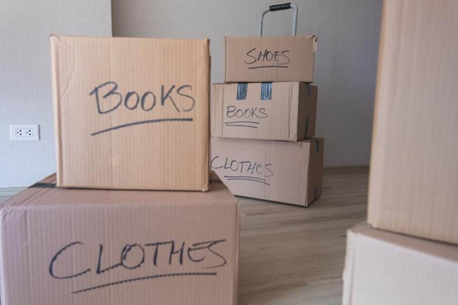 Labeled moving boxes marked “books,” “clothes,” and “shoes” stacked in an empty room.