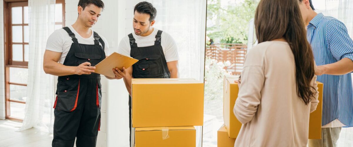 Two movers check a clipboard while helping a family pack and move boxes inside a bright, modern home.
