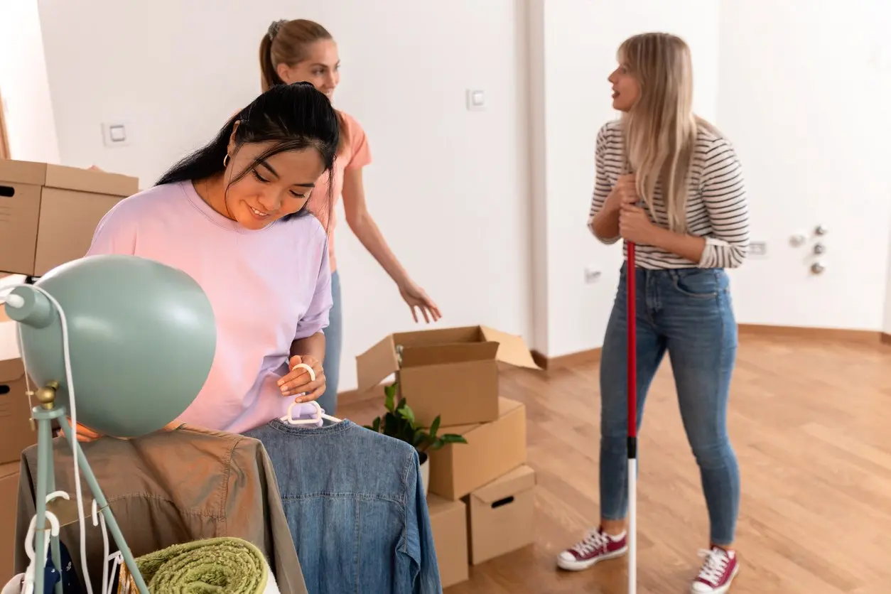 Three young women pack boxes and clean an apartment together while preparing for a move. 