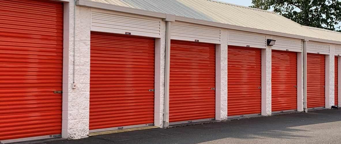A row of outdoor self storage units with bright red roll-up doors and white walls.