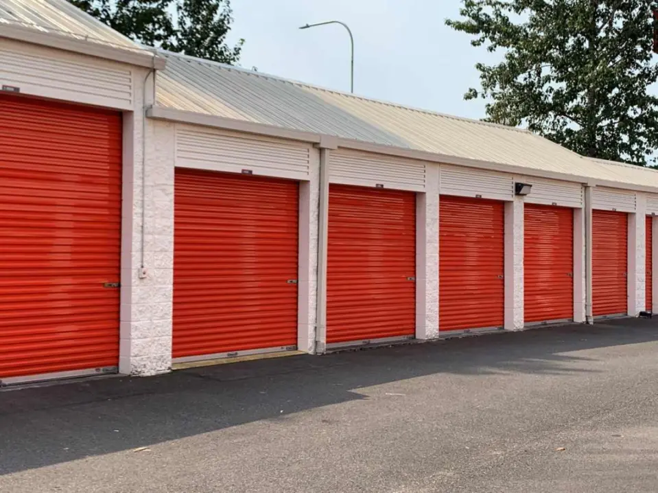 A row of outdoor self storage units with bright red roll-up doors and white walls.