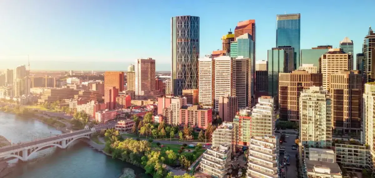 The Downtown Calgary skyline with Bow River and modern high-rise buildings under a clear blue sky at sunset.