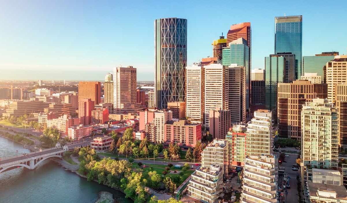 The Downtown Calgary skyline with Bow River and modern high-rise buildings under a clear blue sky at sunset.
