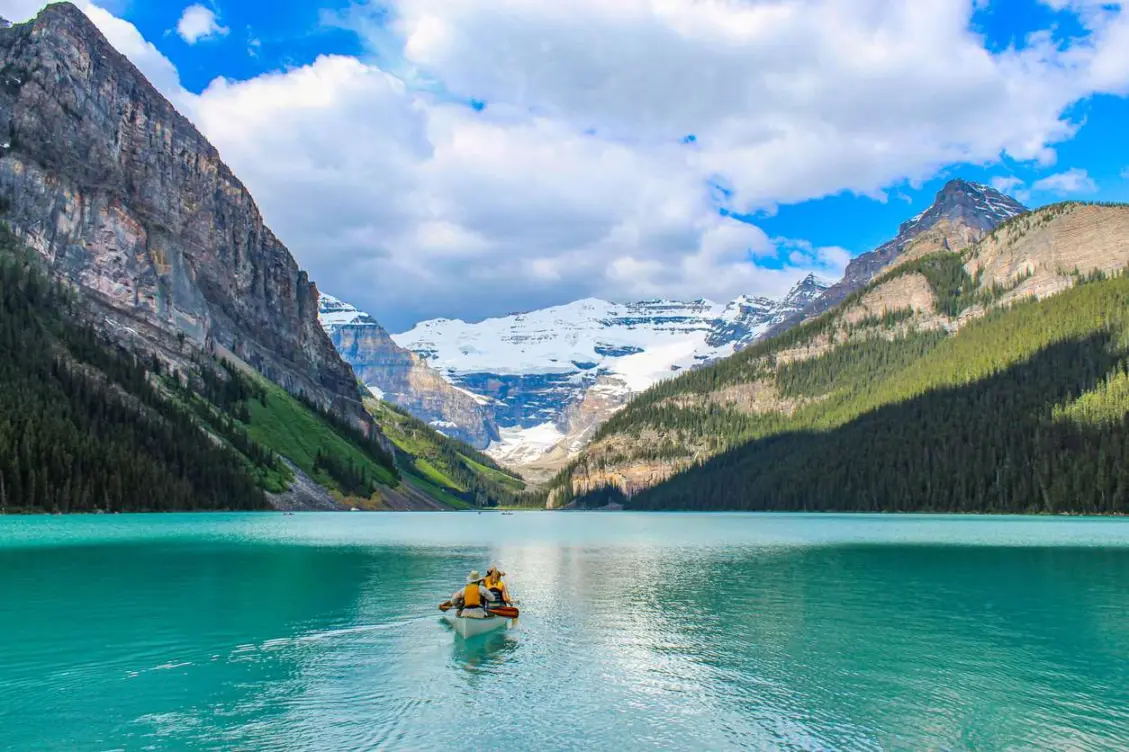 Two people canoeing on the turquoise waters of Lake Louise, surrounded by forested mountains and snowy peaks.